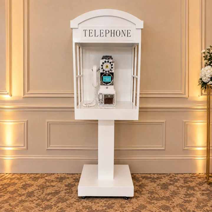 White wedding phone booth with a vintage-style telephone and matching pedestal stand
