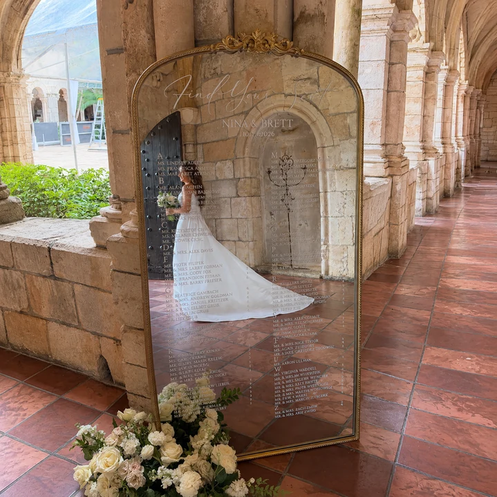 Royal Vinyl Seating Chart with an ornate gold mirror, custom vinyl guest names and table assignments, and a bride reflected in the mirror.